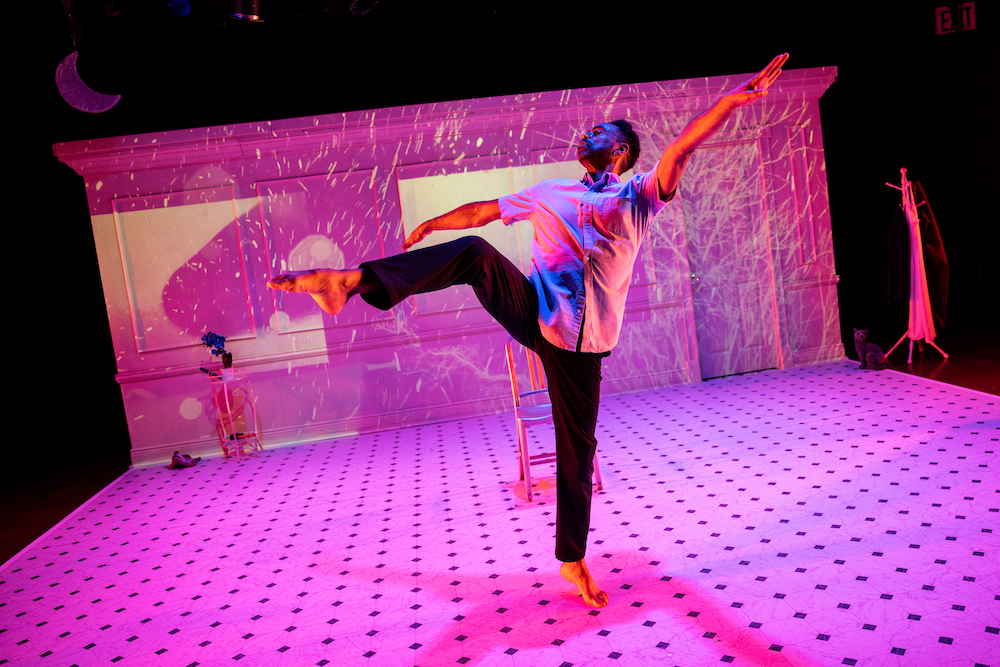 Marcus McGregur kicks one bent leg high showing his fine angles and lines ... he is dancing against a background of pink light